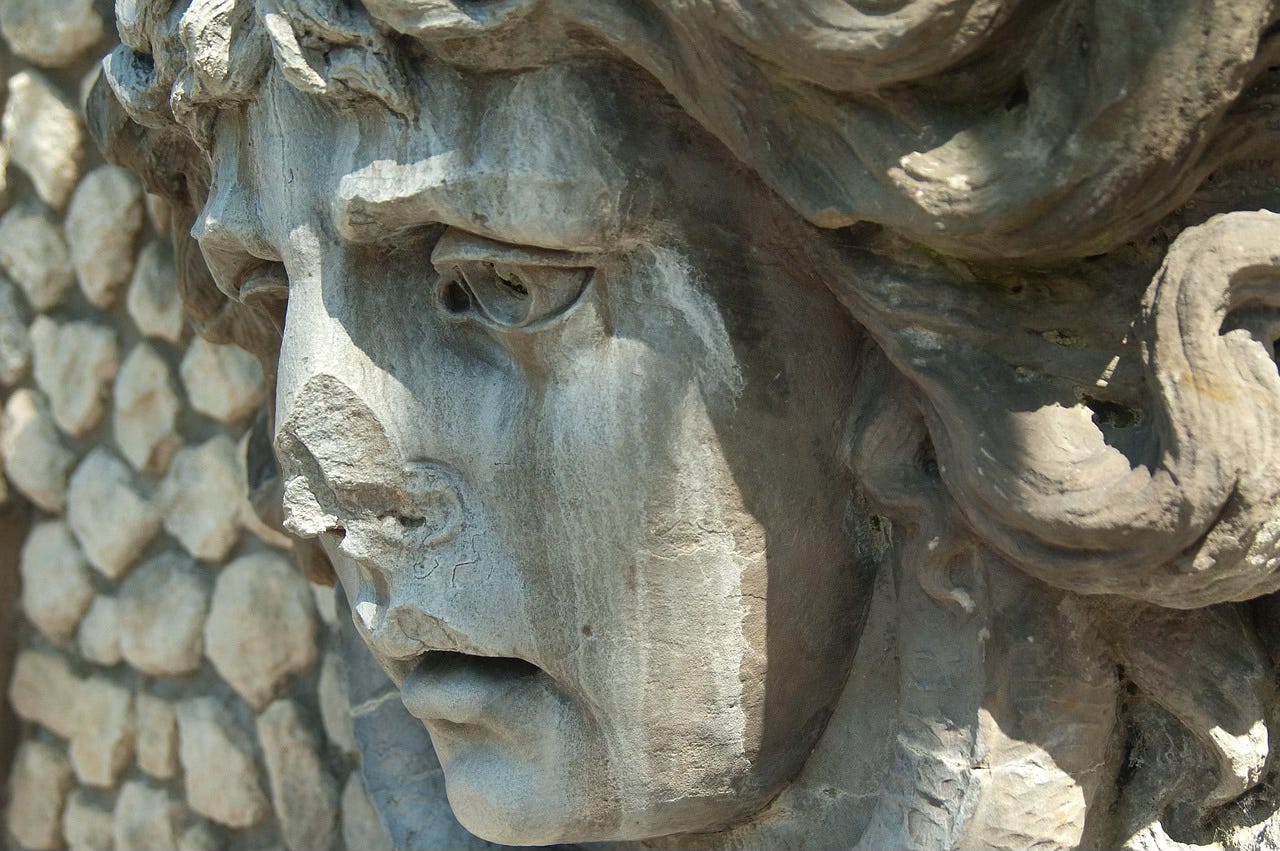 A close-up of a troubled-looking sculpted face in bas-relief. Part of its nose is missing. From somewhere in Frankfurt, Germany.