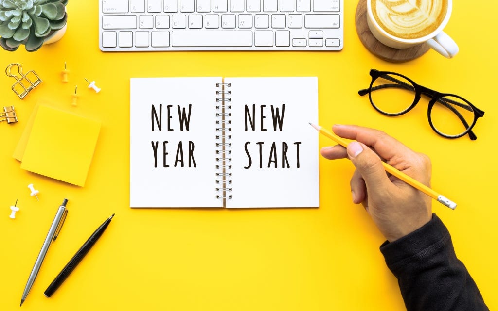 New year new start text with young man writing on notepad on yellow desktop. 