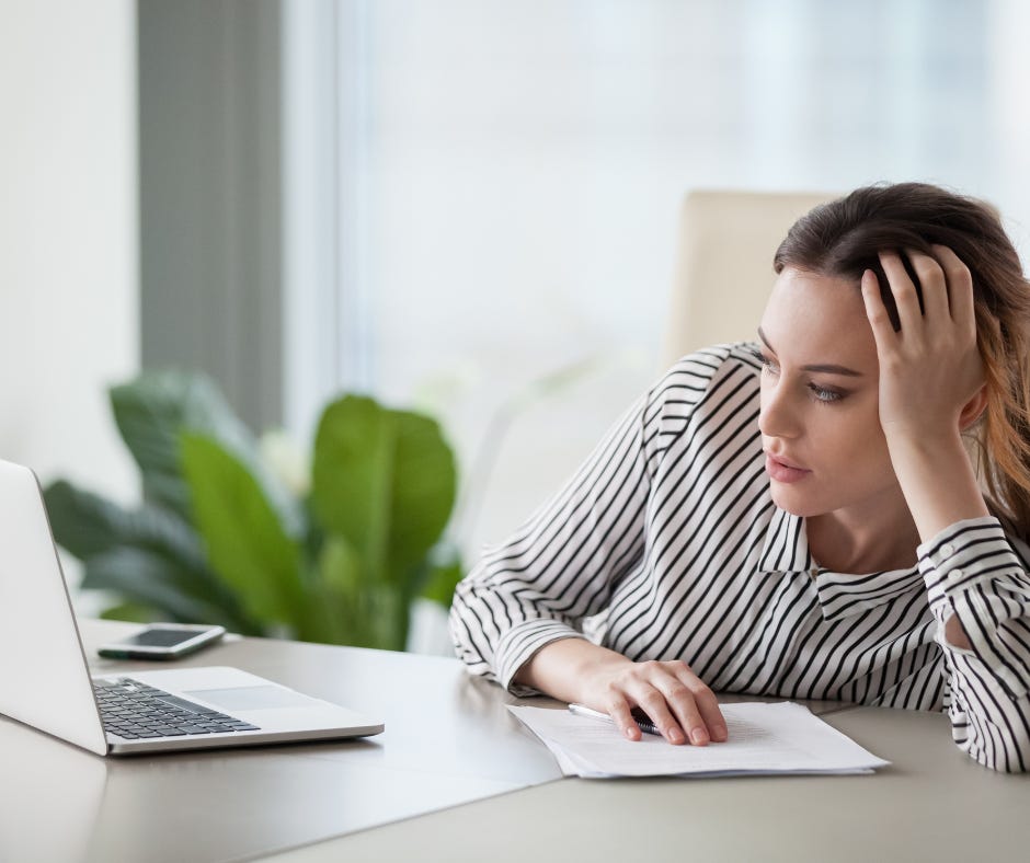 Image of a person sitting at a desk with a laptop, their phone, and their hand holding up their head in a bored stature