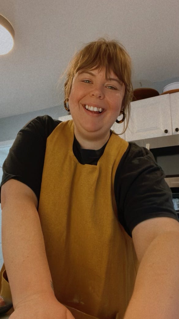 photo of Melissa in a mustard color apron looking down at the camera