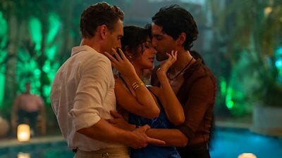 Three people stand by a swimming pool at night in an embrace