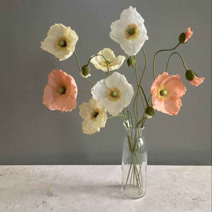 This may contain: an arrangement of white and pink flowers in a glass vase on a marble countertop
