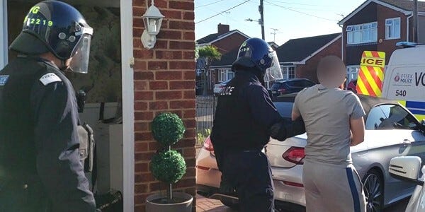Officers leading a handcuffed man from a house towards a police car