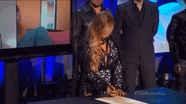 a woman signing a piece of paper with #tidalforall on it