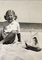 A child sitting on a beach with a toy boat

Description automatically generated