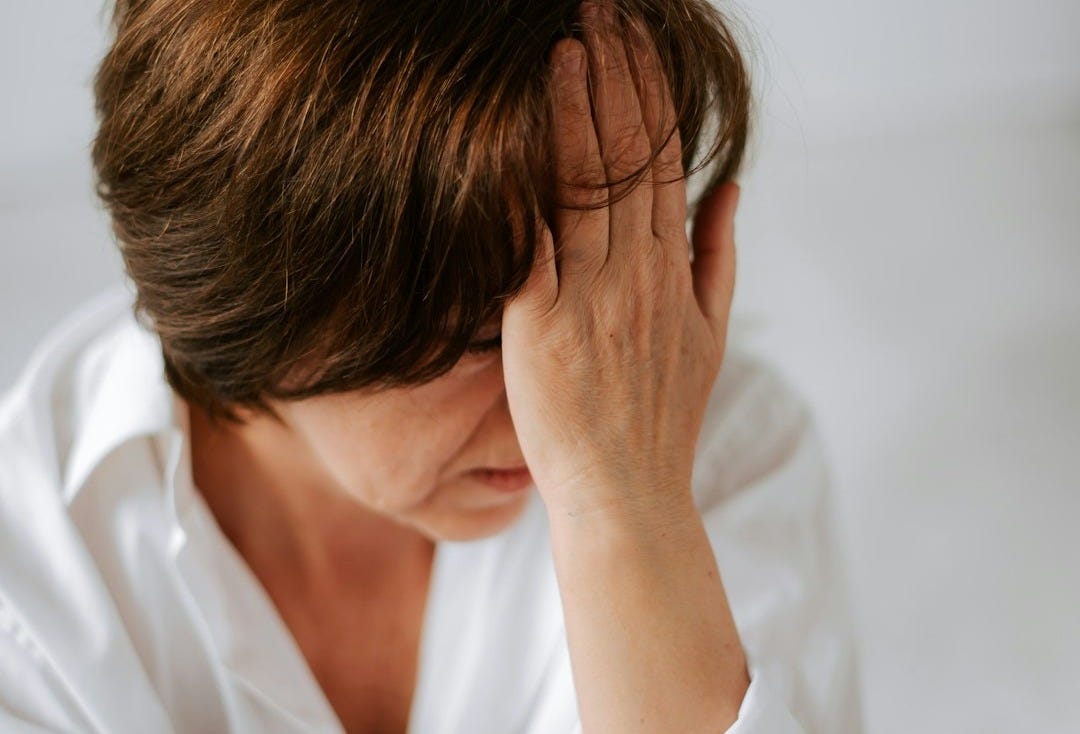 a woman sitting on a bed holding her head in her hands a woman sitting on a bed holding her head in her hands