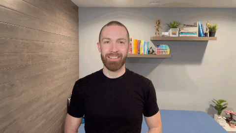 middle-aged white male with facial hair smiling and pointing upwards in front of a bookshelf