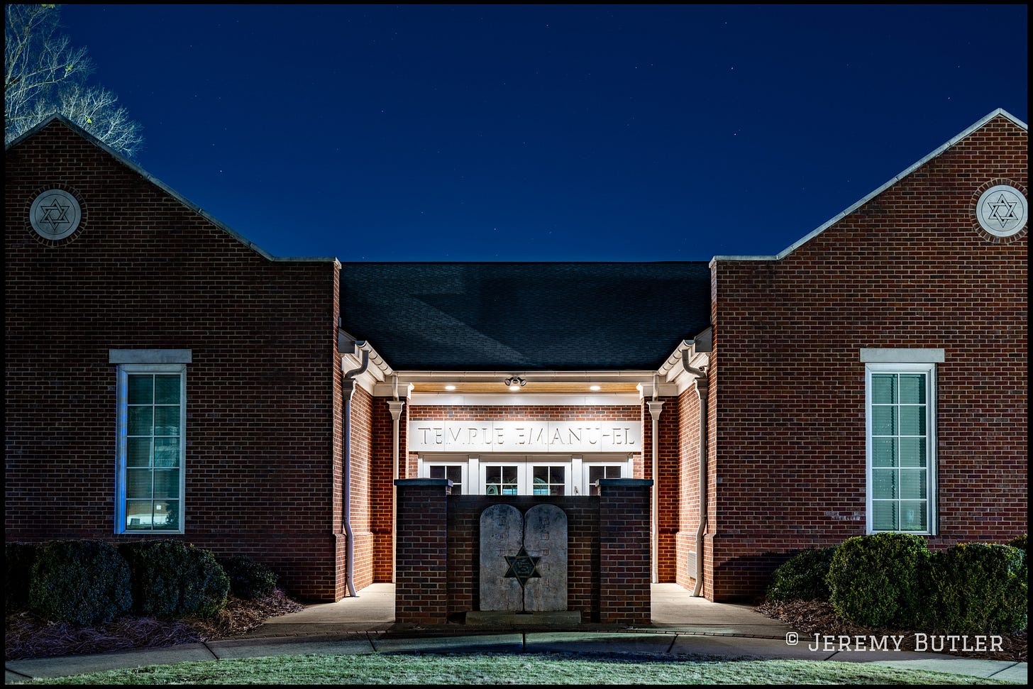 Illuminated red-brick facade of Temple Emanuel synagogue at night with Star of David symbols and entrance monument.