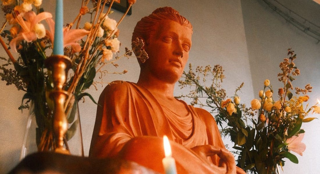 An orange Buddhist statue with flowers and candles either side of it