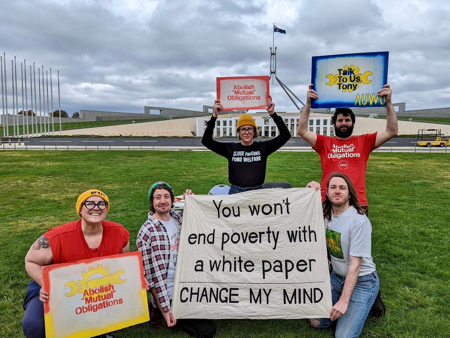Activists outside Parliament House behind a banner that reads “You won’t end poverty with a white paper” and hand made signs that say “Abolish mutual obligations”. Activists outside Parliament House behind a banner that reads “You won’t end poverty with a white paper” and hand made signs that say “Abolish mutual obligations”.
