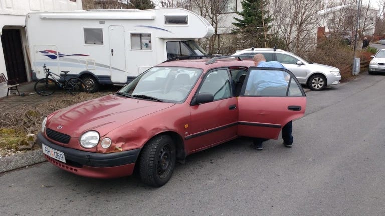 a battered old Nissan with a huge dent on the front fender