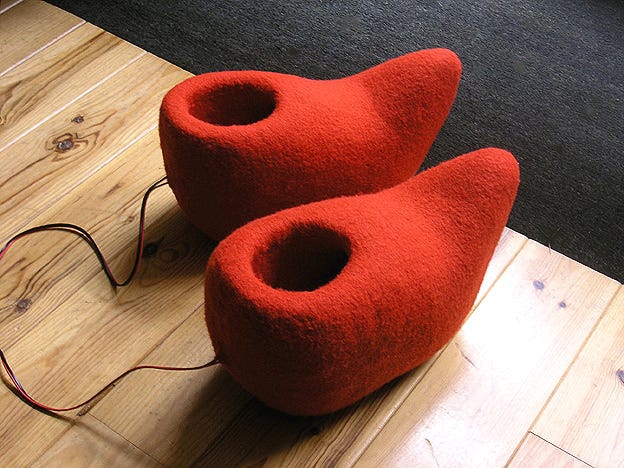 Two enlarged dutch shoes covered in red wool. The heels of the shoes are connected to red and black speaker wires.