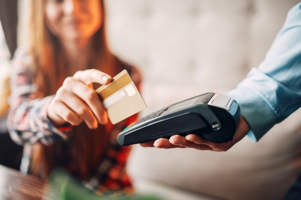 Young woman using a credit card to pay at a cafe, waiter holding payment terminal Young woman using a credit card to pay at a cafe, waiter holding payment terminal