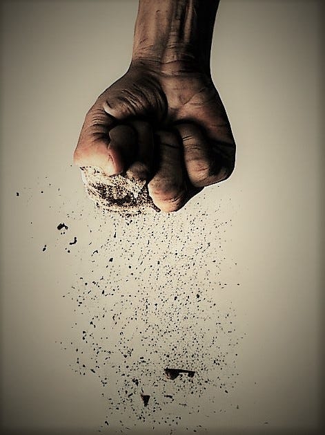 A man's fist releases ash onto the ground