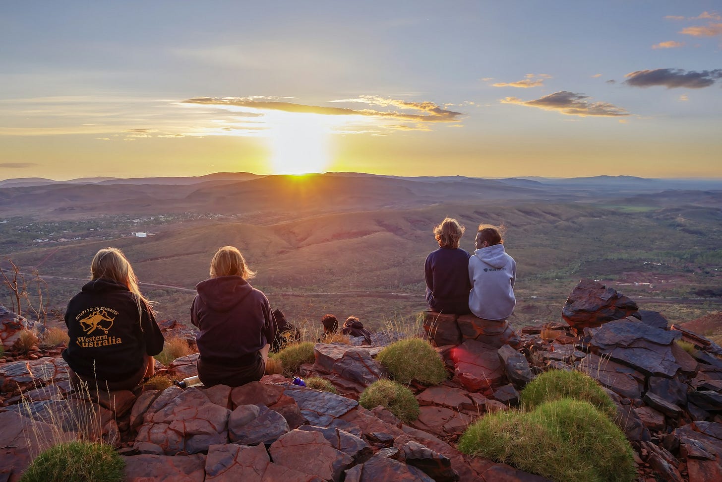four young people watching a beautiful sunset over a vast landscape