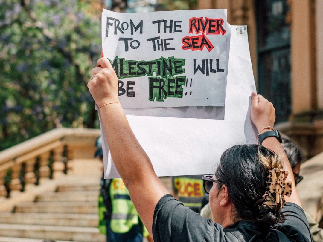 a man holding a sign that says from the river to the sea a man holding a sign that says from the river to the sea