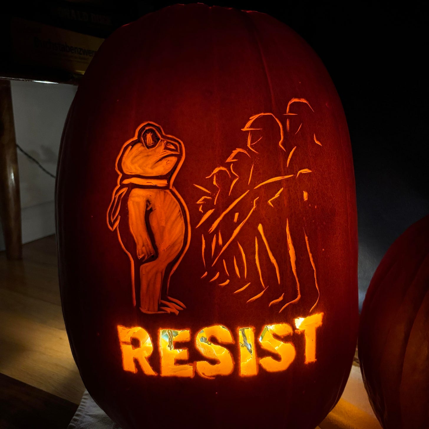 A glowing carved pumpkin featuring a protest-themed design with the word “RESIST” illuminated beneath a group of figures standing in solidarity. The artwork symbolizes courage, activism, and unity in the face of adversity.