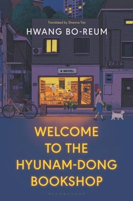 The cover of "Welcome to the Hyunam-dong Bookshop" by Hwang Bo-reum is designed to evoke a sense of warmth and nostalgia, resonating with its literary and reflective themes. It features a cozy bookshop with intricate details, showcasing rows of books and soft, inviting colors that emphasize comfort and serenity. There is a woman walking outside with a cat and a bicycle.