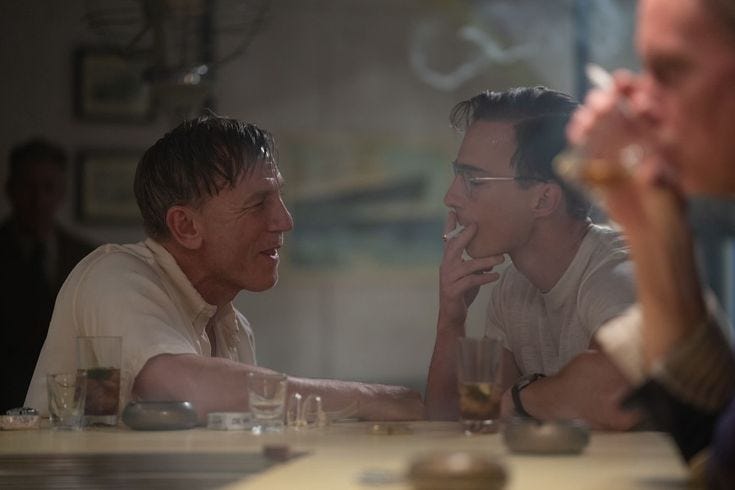 This may contain: two men sitting at a table with drinks in front of them and one man holding his hand up to his mouth