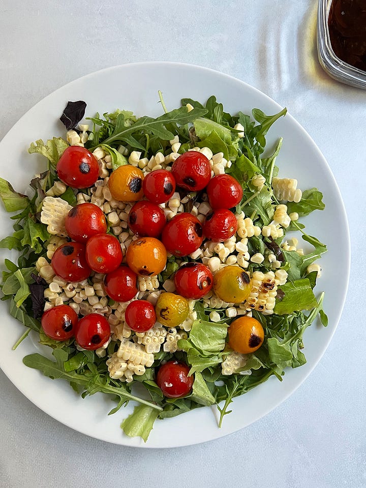 Blistered corn, tomato and arugula salad on white plates.