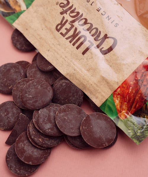 A bag of Luker Chocolate with dark chocolate buttons spilling out, on top of a pink table