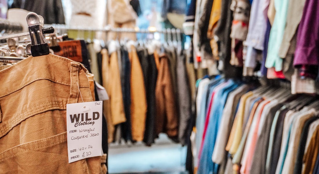 A close-up of a pair of trousers with a price label, with clothes rails behind it