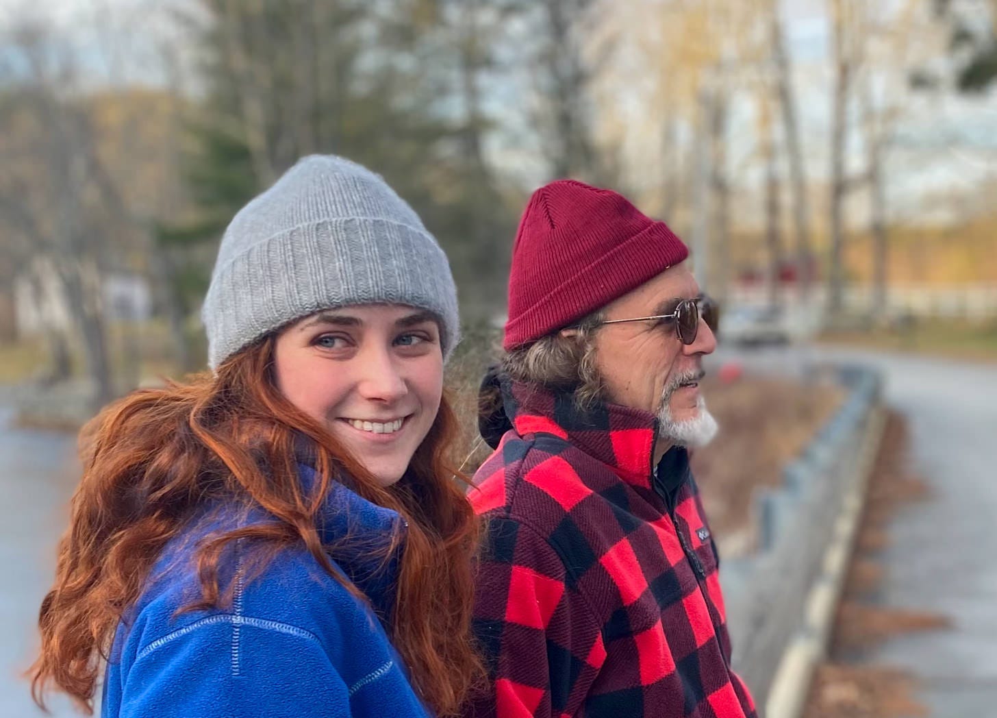 Close up shot of young red haired woman and older man sitting on a low bridge with woods in background