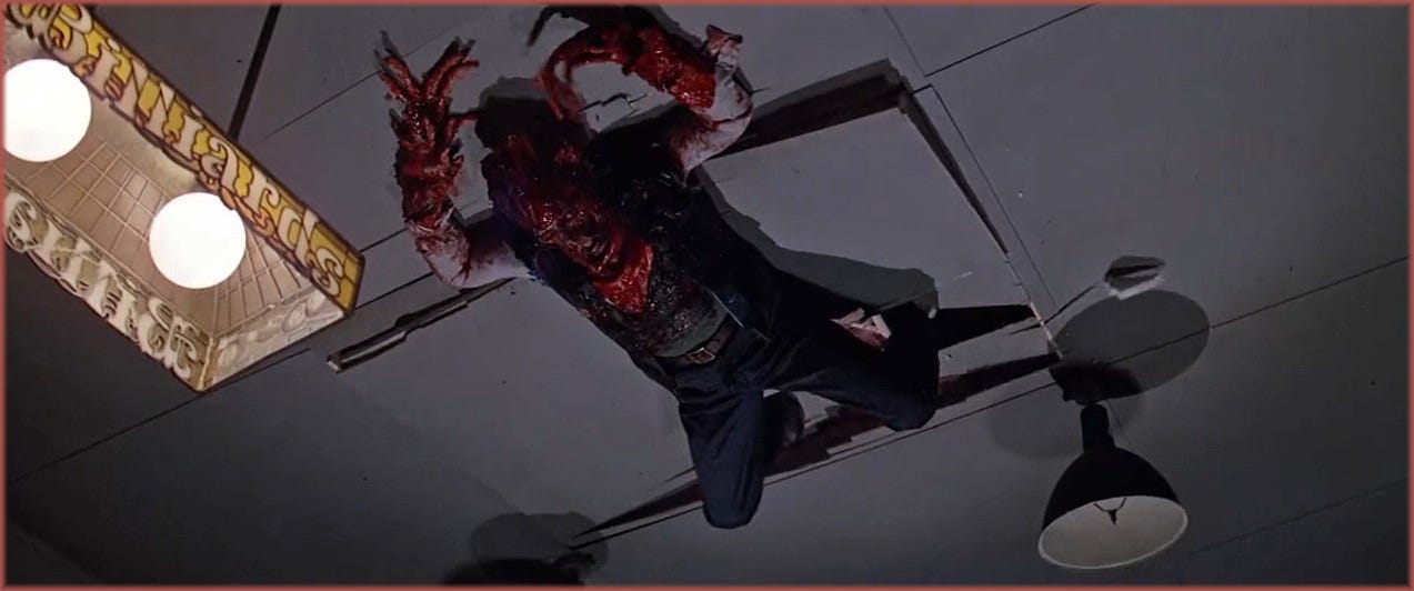 Film frame from The Thing (1982): the Palmer-Thing clinging to the ceiling of the rec room, shot from below on an inverted set. The creature suit was worn by stunt coordinator Dick Warlock. The effect was achieved by turning the set upside down and having Warlock fall onto a mattress covered in balsa wood painted to match the floor.