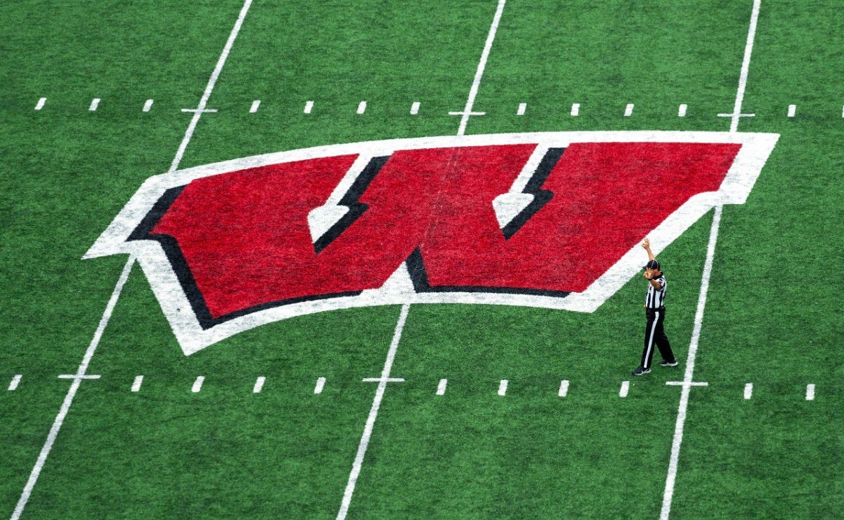 A college football referee raises one arm while walking past the large red Wisconsin “W” logo at midfield inside Camp Randall Stadium. A college football referee raises one arm while walking past the large red Wisconsin “W” logo at midfield inside Camp Randall Stadium.