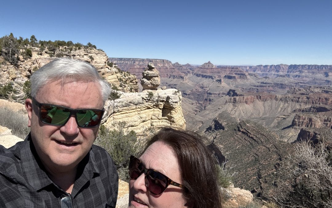 Austin and Betty Gardner smiling together at the South Rim of the Grand Canyon, with the canyon's colorful cliffs and vast landscape stretching behind them during a memorable trip together.