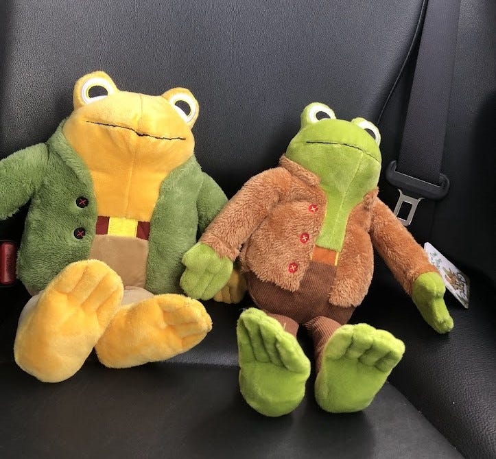 Frog and Toad plushies sitting in the backseat of a car.