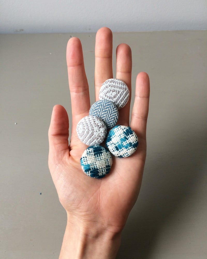 A hand holding five multi-coloured fabric covered buttons in a flat palm