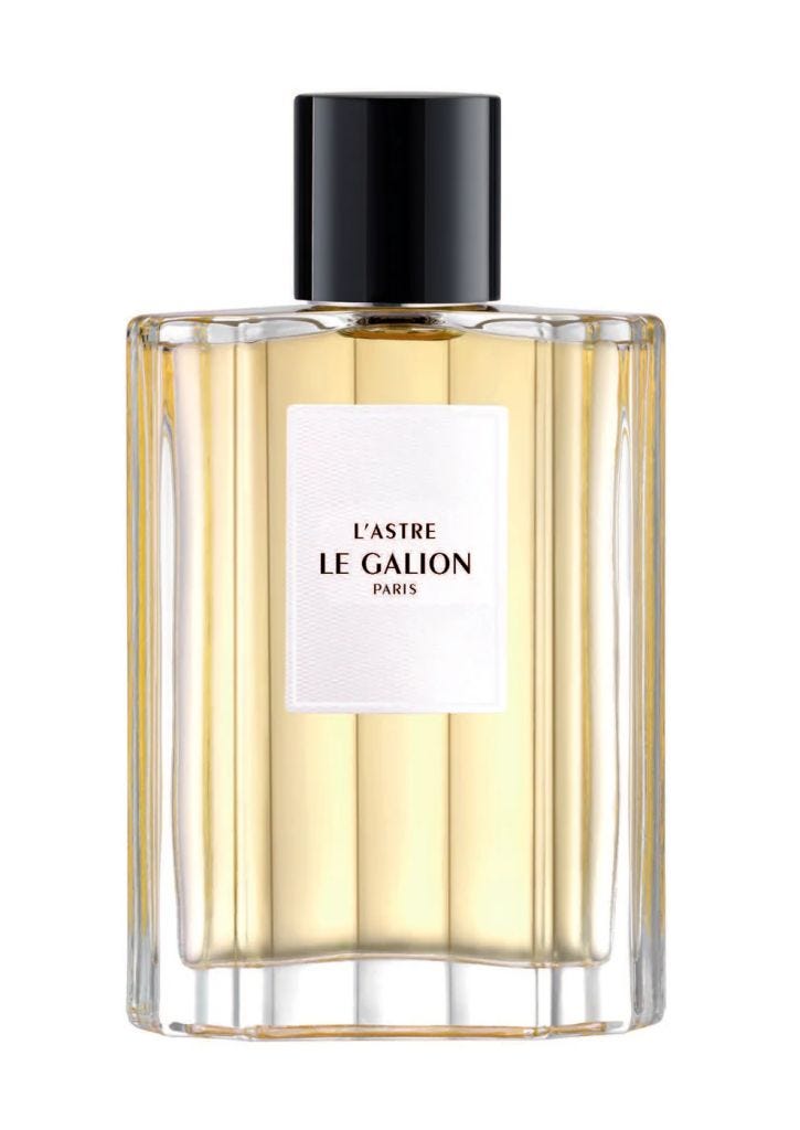 A clear glass bottle of 'L'Astre' perfume by Le Galion, featuring a black cap and a minimalist white label.