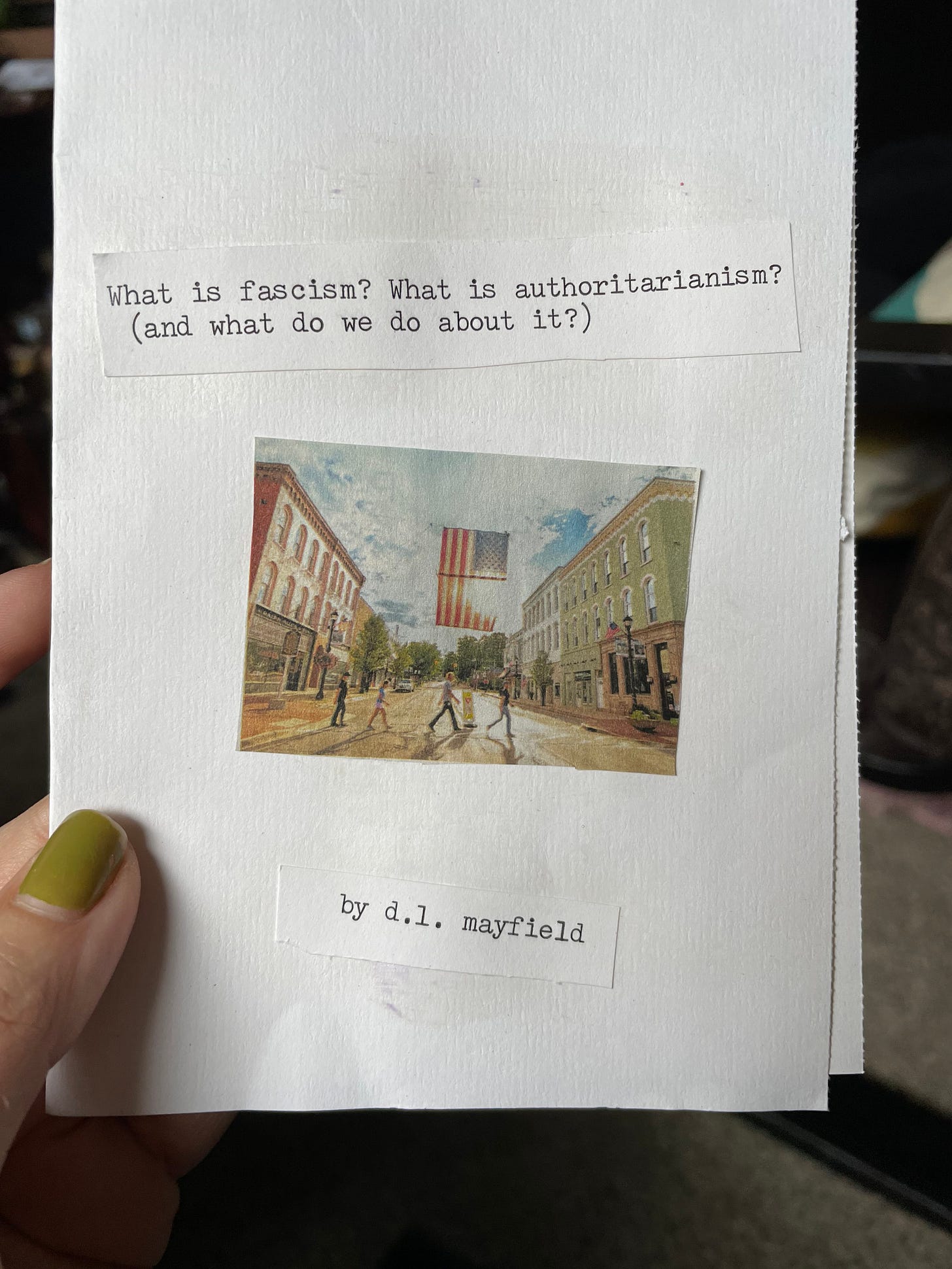 a white paper folded up into a zine. in typewriter text that has been cut and pasted it says What is fascism? What is authoritarianism? (and what do we do about it?) there is an image cut out of a Reader's Digest of an American town with an American flag strung up between two city streets. On the bottom in typewriter type it says by d.l. mayfield