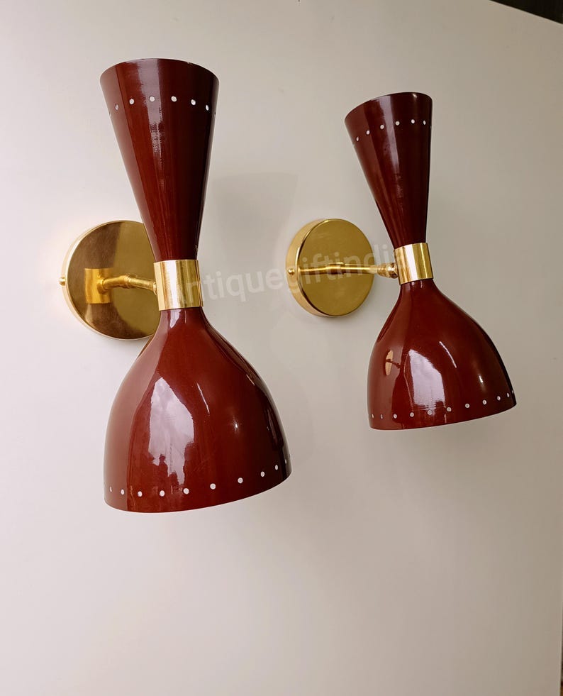 May include: A pair of vintage wall sconces with a brass base and red metal shades. The shades have a dotted pattern and a cone shape. May include: A pair of vintage wall sconces with a brass base and red metal shades. The shades have a dotted pattern and a cone shape.