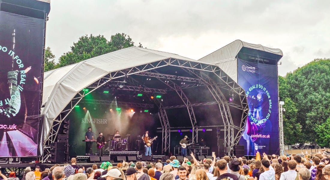 Kingfishr playing on a stage with green and purple lights on it, with a crowd in front of them