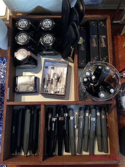 This may contain: an assortment of pens and ink in a wooden box on top of a table with other items