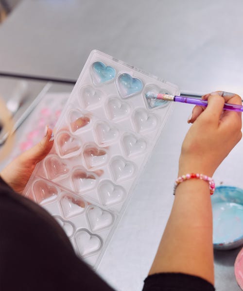 A hand painting a clear chocolate mould with hearts blue