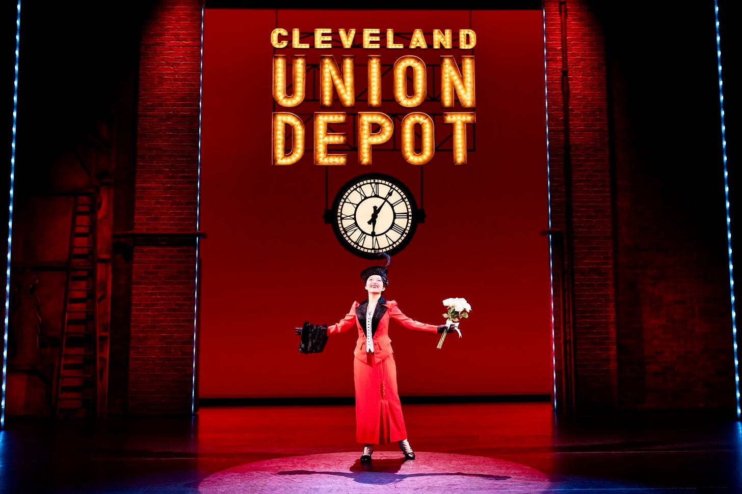 A women stands in a train depot holding a bouquet of flowers