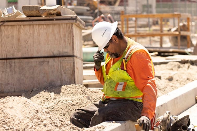 A construction worker sits and puts his head down, still in the hot sun. A construction worker sits and puts his head down, still in the hot sun.