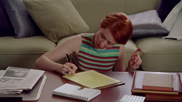 This may contain: a woman sitting at a table writing on a notepad and holding a pen in her hand