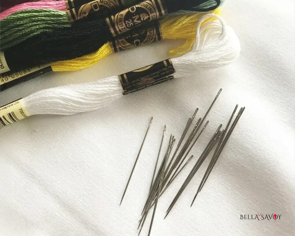 embroidery floss and needles sitting on white cotton fabric