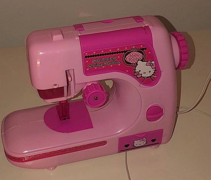 This may contain: a pink hello kitty sewing machine sitting on top of a white table next to a wall