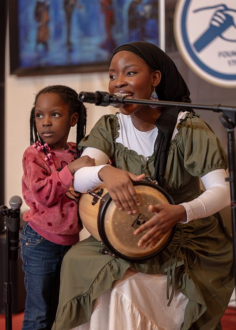 Teledalase singing and playing her hand drum with her child at Delaware Music Network Open Mic.