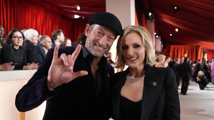 Deaf actors Troy Kotsur and Marlee Matlin are on a red carpet. Troy signs "I love you."