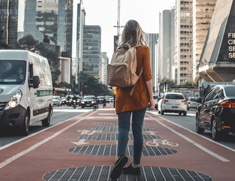 photography of woman walking in between road with vehicles