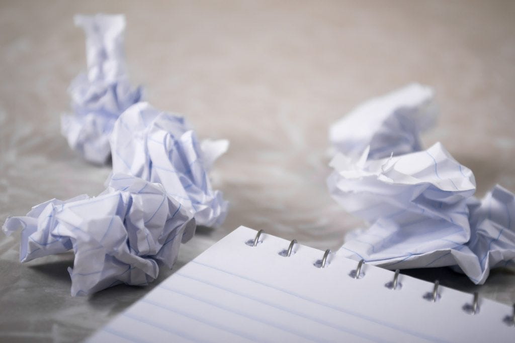 waded up writing paper next to a writing note pad with an empty page showing waded up writing paper next to a writing note pad with an empty page showing