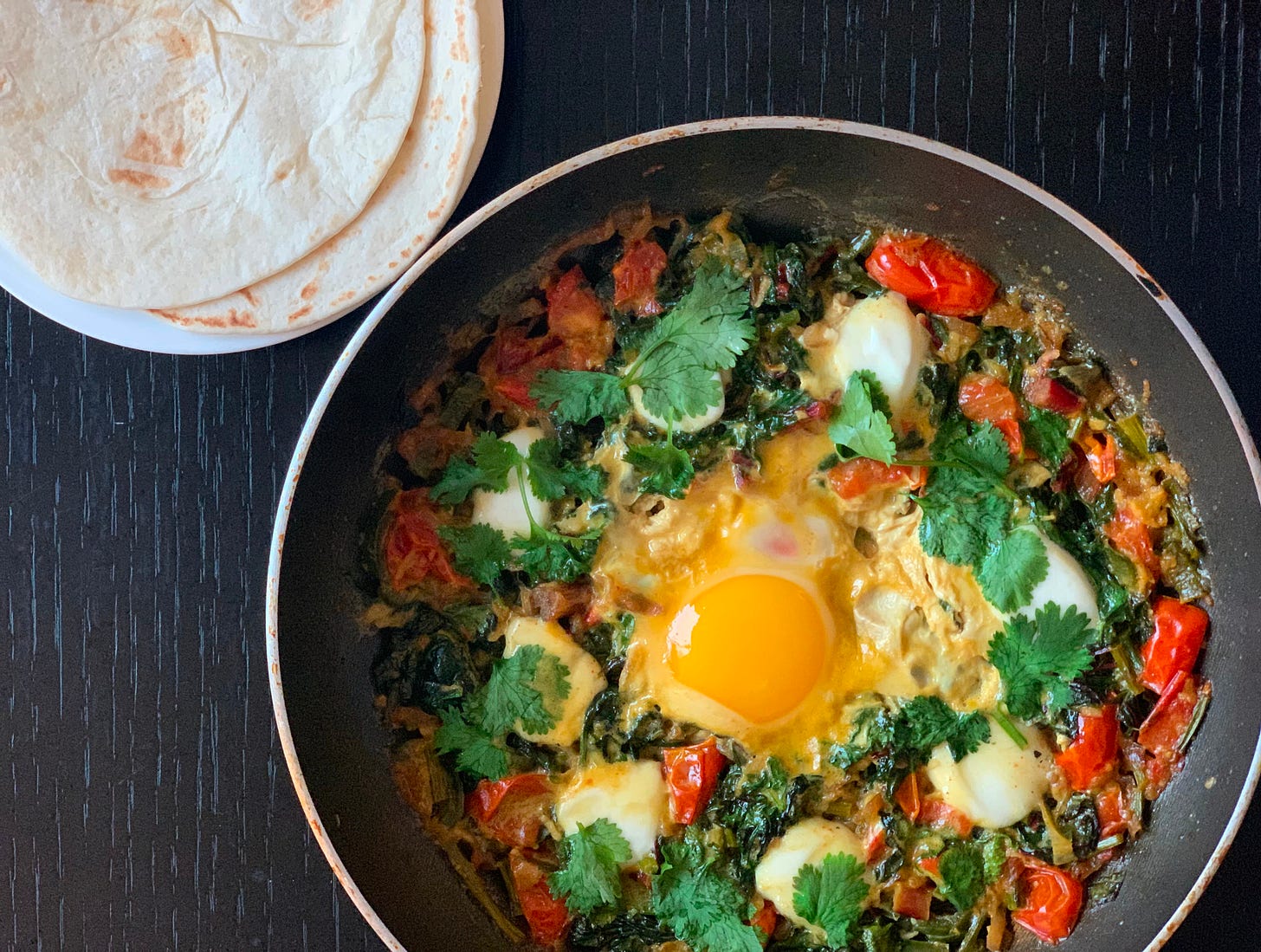 A unique variation of shakshuka, made by Liat Portal for Foodie Disorder, blending sautéed leafy greens with a rich tomato base and perfectly poached eggs. Garnished with fresh cilantro and served in a black pan alongside soft flour tortillas, this dish brings a fresh, herbaceous twist to the classic. Captured as part of The Liat Show, this photo showcases the versatility of shakshuka beyond its traditional form.