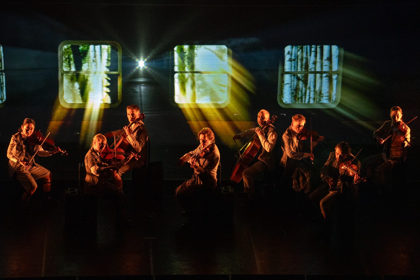 String players performing in what looks like a railway carriage with a forest seen through the windows