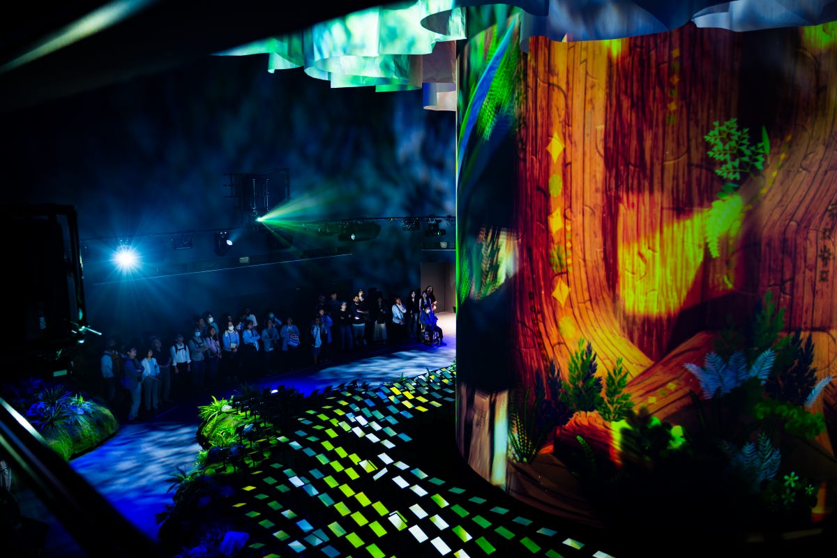 A small group of people gaze up at images of nature projected onto a massive, cylindrical screen in the Tech World pavilion